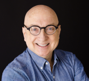 Headshot of Walter Fritz. A bald man with thick rimmed black glasses wearing a chambray button up shirt.