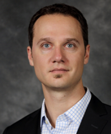 Headshot of Dr. Timothy Wideman. A man with short dark hair, wearing a crosshatch button up shirt with a black suit jacket.